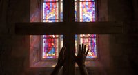Hands raised in prayer silhouette against colorful stained glass church windows creating spiritual atmosphere for worship and meditation concepts.