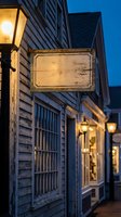 Vintage wooden sign hanging on historic colonial building with lantern lighting at dusk, weathered blank signage for business branding and advertising.
