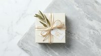 Elegant cream gift box tied with twine bow and olive branch on marble surface, special offer tag, minimal luxury style for holiday and wedding.