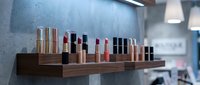 Luxury cosmetics collection displayed on wooden shelf in modern beauty salon or makeup studio interior with professional lighting and clean aesthetic.