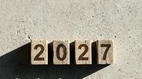 Wooden blocks displaying year 2027 numbers arranged on textured sand surface with natural shadows for business planning and future goals concept.