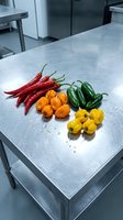 Fresh colorful chili peppers arranged on stainless steel commercial kitchen counter for culinary preparation and cooking ingredients display.