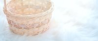 Empty wicker basket on soft white fur background for home decor, storage solutions, and rustic interior design projects.
