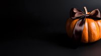 Orange pumpkin with elegant brown satin ribbon bow on black background, creating dramatic contrast for autumn seasonal decoration.