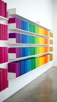 Colorful rainbow books arranged on white floating shelves creating vibrant spectrum display for modern library interior design and home organization.