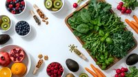 Fresh organic vegetables and fruits arranged on white background with spinach, berries, avocado, kiwi, pomegranate for healthy eating and nutrition.