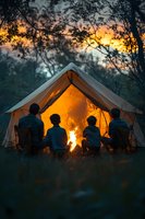 Family sitting by campfire outside illuminated tent at sunset, silhouettes against warm glow creating cozy outdoor atmosphere for camping and adventure lifestyle.