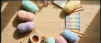Colorful yarn balls arranged in circle with knitting needles and tea cup on wooden floor. Crafting hobby supplies for handmade projects and creative activities.