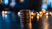 Stack of shiny coins on dark wooden surface with soft bokeh lights in background creating atmospheric financial concept for savings and investment.