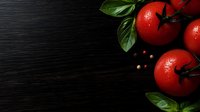Fresh ripe tomatoes with water drops and basil leaves on dark wooden background with peppercorns, copy space for menu or recipe design.