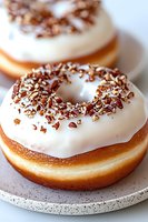 Fresh baked donuts with white glaze icing and crushed pecan nuts topping on speckled ceramic plate, close up view showing texture and layers.