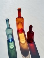 Colorful glass bottles casting vibrant shadows in blue, amber and red tones on white surface, minimalist composition with dramatic lighting for creative design projects.