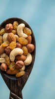 Mixed nuts and dried fruits in wooden spoon on blue background. Healthy snacking, protein rich food, natural nutrition concept for wellness lifestyle.