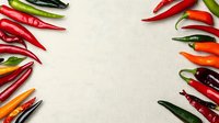 Fresh colorful chili peppers arranged in frame border on white linen textile background, copy space in center for text or design elements.