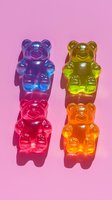 Colorful gummy bear candies on pink background with harsh shadows. Blue, yellow, red and orange translucent jelly bears arranged in vertical line.