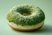 Fresh baked donut covered with green matcha powder and white cream filling on mint green background, close up view of sweet pastry dessert.