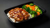 Glazed teriyaki chicken over steamed rice with fresh broccoli and carrots in black takeout container for meal prep and healthy dining options.