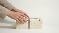 Hands placing elegant marble-textured gift box on clean surface, luxury packaging concept for premium products and special occasions.