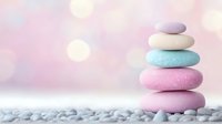 Balanced pastel colored zen stones stacked on pebble surface against soft pink bokeh background, representing wellness, meditation and spa atmosphere.