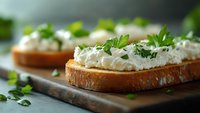 Fresh herb cream cheese spread on toasted bread slices garnished with microgreens on wooden cutting board for healthy breakfast or appetizer recipes.