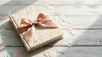 Elegant gift box with pink satin ribbon bow on rustic white wooden background surrounded by colorful paper confetti circles for celebrations and holidays.