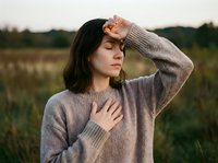 Young woman in cozy sweater touching forehead with closed eyes in peaceful outdoor setting during golden hour for wellness and mindfulness concepts.