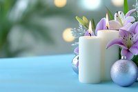 Elegant holiday composition with white candles, purple lilies, and silver ornaments on turquoise surface against blurred bokeh background.