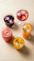 Colorful fruit cocktails and mocktails with ice cubes, berries and citrus garnishes on wooden background for summer refreshment and party beverages.