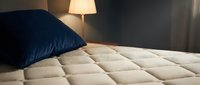Cozy bedroom corner featuring a quilted mattress with navy blue pillow and warm bedside lamp lighting, perfect for home decor and hospitality design projects.