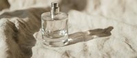 Transparent glass perfume bottle with spray atomizer on beige linen fabric, casting soft shadow, suitable for fragrance marketing and cosmetic product advertising.
