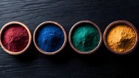 Vibrant natural powder pigments in wooden bowls arranged in row showing red, blue, green and yellow colors on dark wooden background. Perfect for art and design projects.