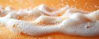 Flowing white foam and bubbles on orange liquid surface creates dynamic texture with splashing droplets and frothy waves in macro photography.