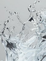 Dynamic water splash with crystalline droplets and flowing liquid motion captured in high-speed photography against light gray background.