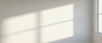 Sunlight streaming through window panes casts geometric shadows on neutral beige wall, creating minimalist interior design backdrop for product placement and branding.