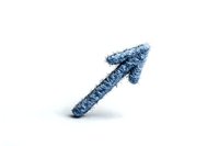 Upward pointing blue denim arrow made from recycled jeans fabric on white background, isolated creative symbol for growth, success and sustainability.