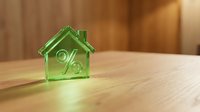 Green transparent house model with percentage symbol on wooden surface representing mortgage rates, real estate investment and property financing concepts.