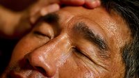 Middle-aged man receiving relaxing facial massage at spa with hands gently massaging face and forehead for wellness and stress relief treatment.