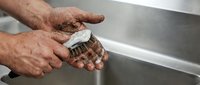 Senior man washing hands with soap and brush at kitchen sink for hygiene and cleanliness routine.