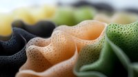 Macro view of colorful textured fabric with perforated pattern showing black, peach and green wavy folds in soft light, creating abstract minimalist design.