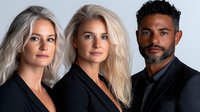Professional diverse business team portrait with two blonde women and bearded African American man in black attire against light studio background.