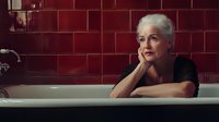Elegant mature woman with silver hair relaxing in vintage bathtub against burgundy tile wall, wearing black top, contemplative atmospheric portrait.