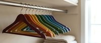 Colorful wooden coat hangers arranged on closet rod displaying rainbow spectrum from brown to blue for organized wardrobe storage and home organization.
