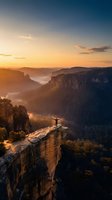 Adventurous hiker standing on dramatic cliff edge overlooking vast canyon landscape at golden hour sunrise with arms raised in triumph and freedom.