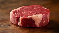 Fresh raw ribeye steak with marbling on wooden cutting board, close up view of premium beef cut showing rich red meat texture and white fat streaks.