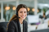 Smiling young female customer service representative with headset in modern office environment, providing professional support.