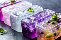 Colorful fruit ice cubes with berries and mint in transparent containers on dark background, perfect for summer refreshments.