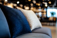 Soft velvet cushions in navy blue and cream colors on modern gray sofa against blurred bokeh lights background, creating cozy home atmosphere.