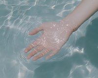 Caucasian hand submerged in clear turquoise water creating gentle ripples, conveying tranquility, relaxation, and connection with nature in spa or wellness setting.