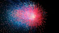 Vibrant red and blue firework explosion against dark night sky creates dramatic starburst pattern with glowing sparks and trails radiating from central burst point.