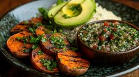 Grilled sweet potato slices with fresh herb quinoa salad and avocado halves on rustic plate for healthy vegetarian meal preparation and clean eating.